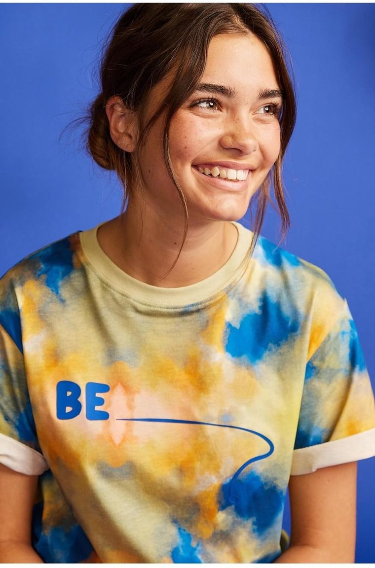 A model wearing the BE.Kids tie-dye tee against a cobalt-blue backdrop