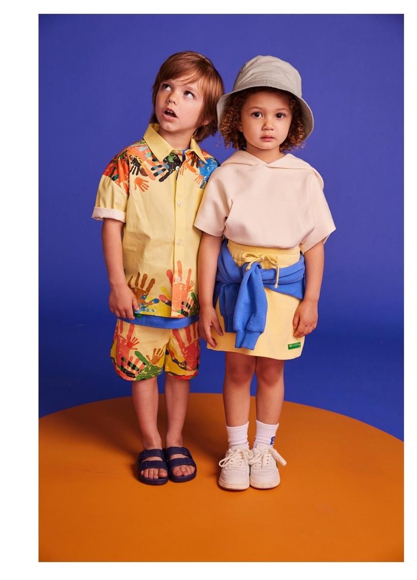 Two young BE.Kids models in printed and pastel looks on a cobalt-and-orange studio set