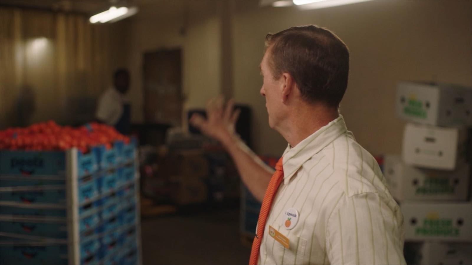 John Birk raising a hand in the supermarket backroom, beside a stacked pallet of Peelz mandarin crates
