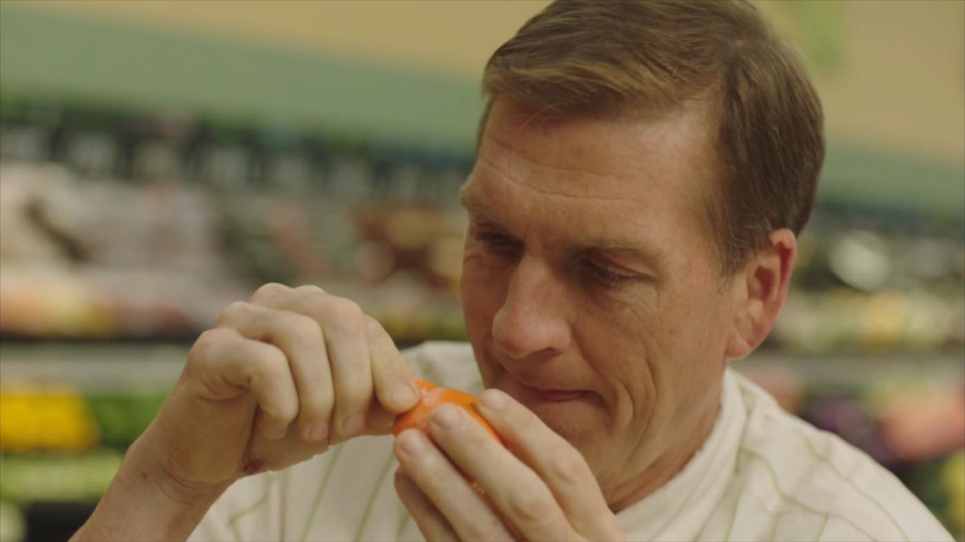 Close-up of John Birk carefully peeling a single mandarin, mid-performance on the produce floor