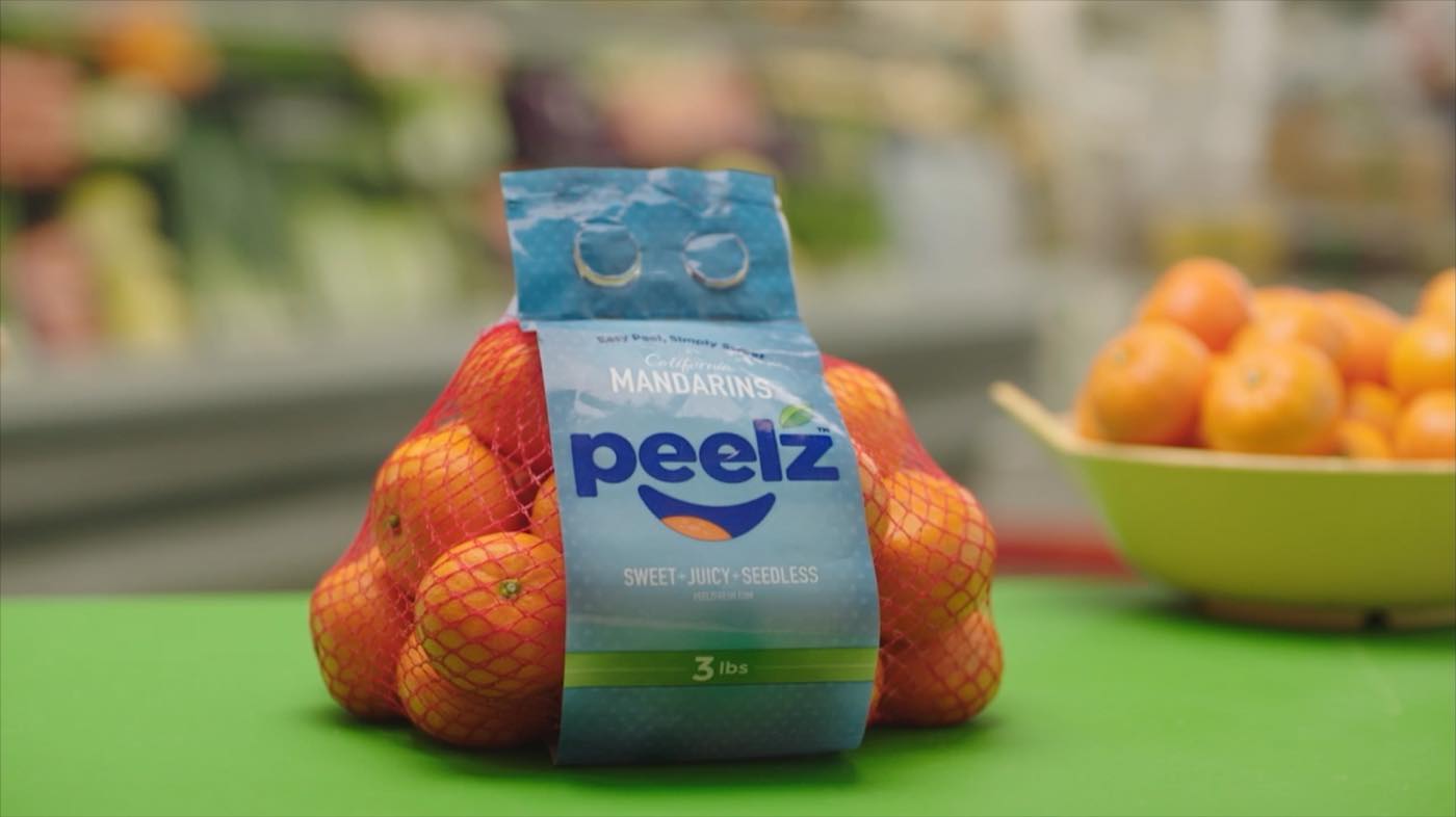A three-pound bag of Peelz California mandarins standing on a green surface with a bowl of loose mandarins behind it